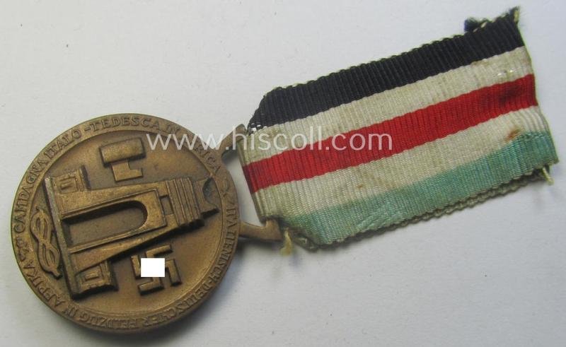 Golden-bronze-coloured- (and I deem 'Buntmetall'-based-) example of a: 'Deutsch-Italienische Feldzugsmedaille' (or: German-Italian campaign-medal) that comes mounted onto its (regular-sized) piece of original (and minimally faded!) ribbon — image 3