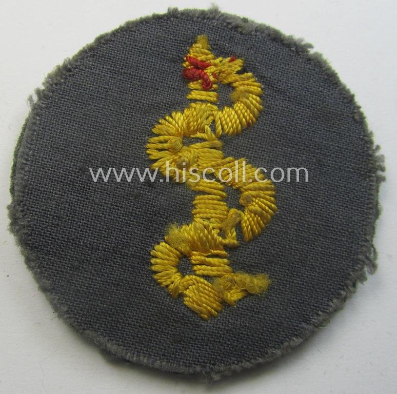 Clearly used- and/or tunic-removed WH (Heeres) so-called: trade- and/or special-career arm-insignia as was intended for a: 'Sanitäter' being a neatly hand-embroidered specimen on a field-grey-coloured background — image 2